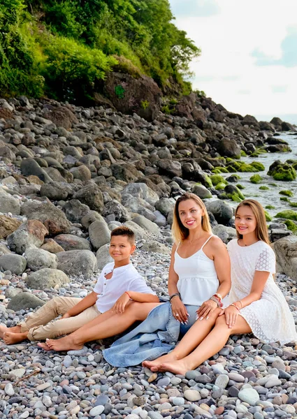 幸せな母親 息子と娘の石の海のビーチで休む 海岸線で楽しい白い服の家族 夏の日と休暇の時間の概念 — ストック写真