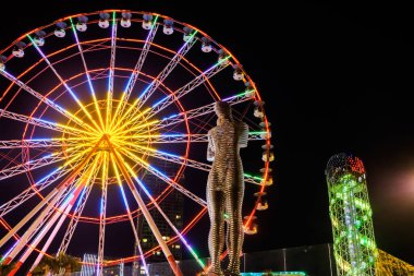 Batumi, Adjara - 20 Haziran 2019. Geceleyin Ali ve Nino 'nun heykeli. Şehir renkli ışıklar ve büyük dönme dolap. Arkaplanda alfabe kulesi.
