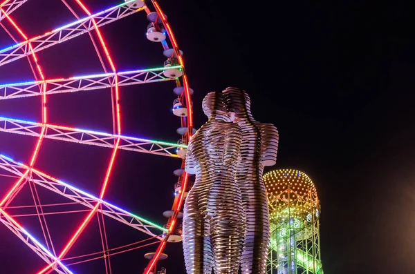 Batumi, Adjara - 20 Haziran 2019. Geceleyin Ali ve Nino 'nun heykeli. Şehir renkli ışıklar ve büyük dönme dolap. Arkaplanda alfabe kulesi.