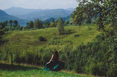 Mutlu, esmer kız çimlerde koşuyor. Arka planda Karpatlar var. Dağda uzun, ipek, yeşil elbiseli romantik bir kadın..