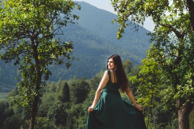 Mutlu, esmer kız çimlerde gülümsüyor. Arka planda Karpatlar var. Dağların ve doğanın güzel manzarası.