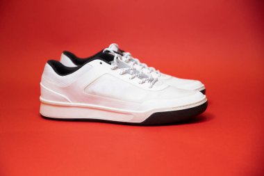 Kırmızı arka planda bir çift modaya uygun beyaz spor ayakkabı. Rahat ve şık ayakkabılar..