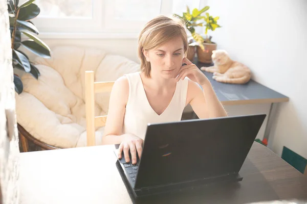A woman in home clothes works on a computer in front of a monitor in a home atmosphere. Flexible working hours and remote work. Clouse-up