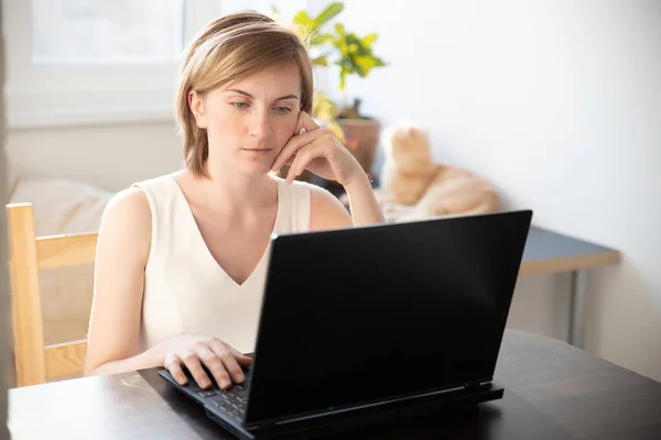 A woman in home clothes works on a computer in front of a monitor in a home atmosphere. Flexible working hours and remote work. Clouse-up