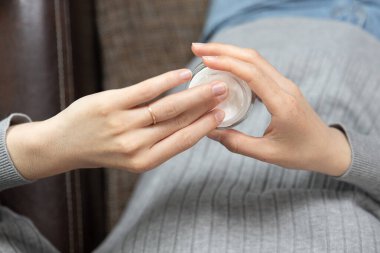 Evdeki yatakta otururken krem süren güzel genç bir kadının kırpılmış görüntüsü.