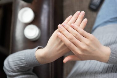 Evdeki yatakta otururken krem süren güzel genç bir kadının kırpılmış görüntüsü.