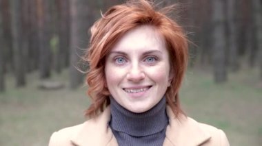 Çekici kızıl saçlı, şık montlu genç bir kadın ormanda yürüyor. Kız gülüyor ve güneşli bahar havasının tadını çıkarıyor. Kapatmak için. Salgından kurtulmak için. Temiz hava..