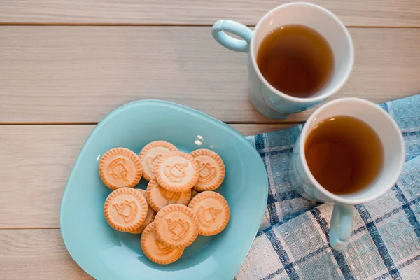 Duas chávenas de chá num guardanapo azul. Biscoitos em uma placa azul em um fundo de madeira — Fotografia de Stock