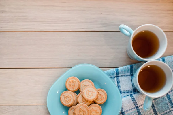 Zwei Tassen Tee auf einer blauen Serviette. Kekse auf blauem Teller auf hölzernem Hintergrund — Stockfoto