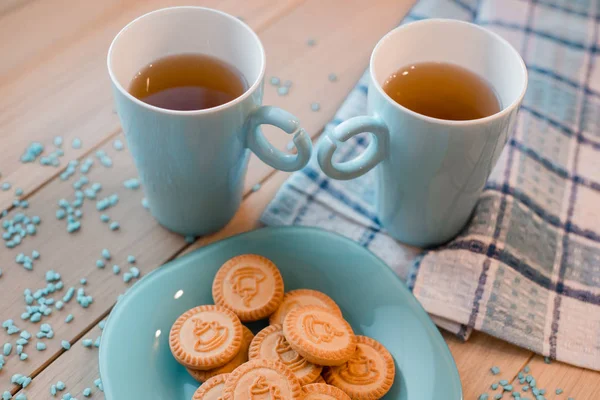 Dos tazas de té en una servilleta azul. Galletas sobre un plato azul sobre un fondo de madera — Foto de Stock