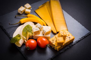 Kalıp, cherry domates, fesleğen ve melissa Yeşiller, kırmızı acı biber koyu gri arka plan üzerinde taş bir tepsi ile peynir