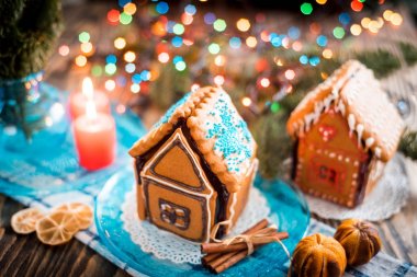 Ev yapımı Noel kurabiye evi bir tabloda görüntülenir. Noel ağacı ışıkları içinde belgili tanımlık geçmiş.