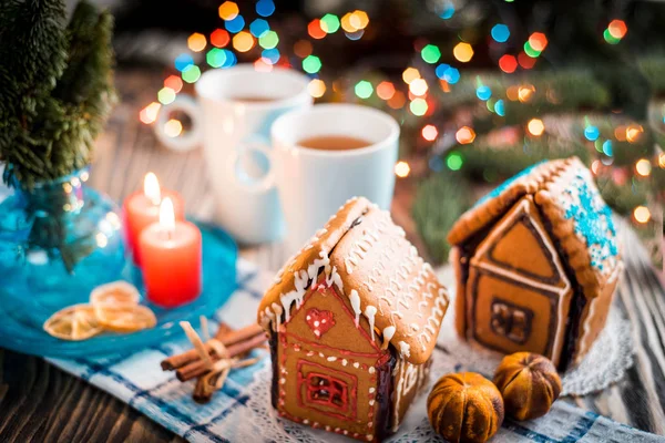 Ev yapımı Noel kurabiye evi bir tabloda görüntülenir. Noel ağacı ışıkları içinde belgili tanımlık geçmiş.