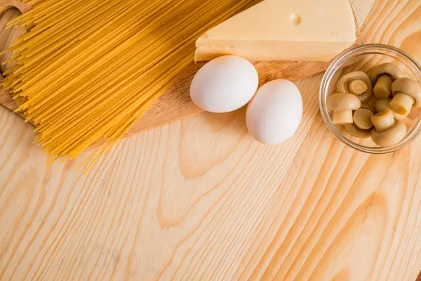 Preparación de espaguetis con champiñones de queso. Huevos y salsa de crema agria, champiñones en una tabla de cortar sobre un fondo de madera — Foto de Stock