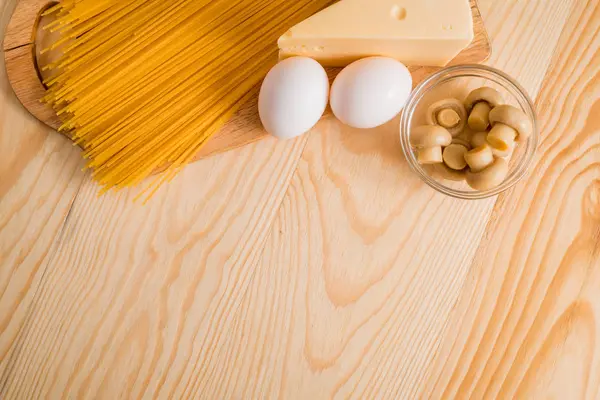 Preparación de espaguetis con champiñones de queso. Huevos y salsa de crema agria, champiñones en una tabla de cortar sobre un fondo de madera — Foto de Stock