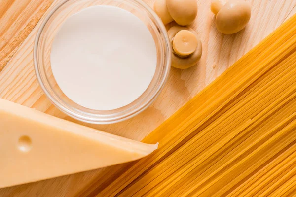 Preparación de espaguetis con champiñones de queso. Huevos y salsa de crema agria, champiñones en una tabla de cortar sobre un fondo de madera — Foto de Stock