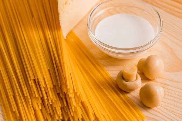 Preparación de espaguetis con champiñones de queso. Huevos y salsa de crema agria, champiñones en una tabla de cortar sobre un fondo de madera — Foto de Stock