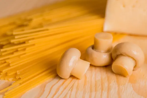 Preparación de espaguetis con champiñones de queso. Huevos y salsa de crema agria, champiñones en una tabla de cortar sobre un fondo de madera — Foto de Stock