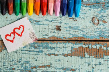 Parlak kalem bir eski mavi yeşil ahşap arka plan üzerinde renkli. Kağıt bir dilim boyalı iki kırmızı kalp