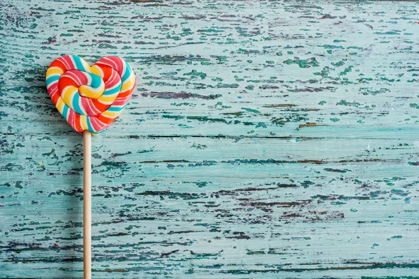 Doces de arco-íris listrado de cor doce em um pau na forma de um coração. em um fundo de madeira vintage verde velho azul. O conceito para o Dia dos Namorados . — Fotografia de Stock