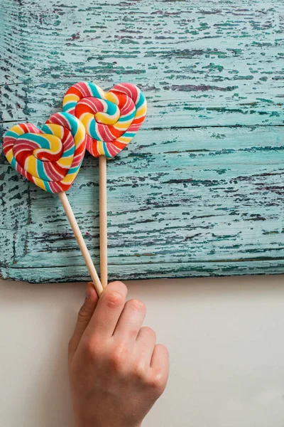 Dois doces de arco-íris listrados coloridos em um pau na forma de um coração. em um fundo de madeira vintage velho azul. O conceito para o Dia dos Namorados . — Fotografia de Stock