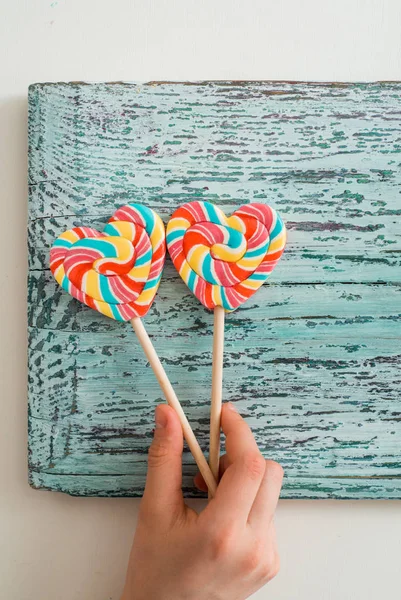 Dois doces de arco-íris listrados coloridos em um pau na forma de um coração. em um fundo de madeira vintage azul. O conceito para o Dia dos Namorados . — Fotografia de Stock