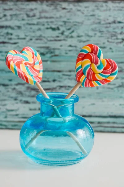 Dois doces de arco-íris listrados coloridos em um pau na forma de um coração. em um fundo de madeira vintage velho azul. O conceito para o Dia dos Namorados . — Fotografia de Stock