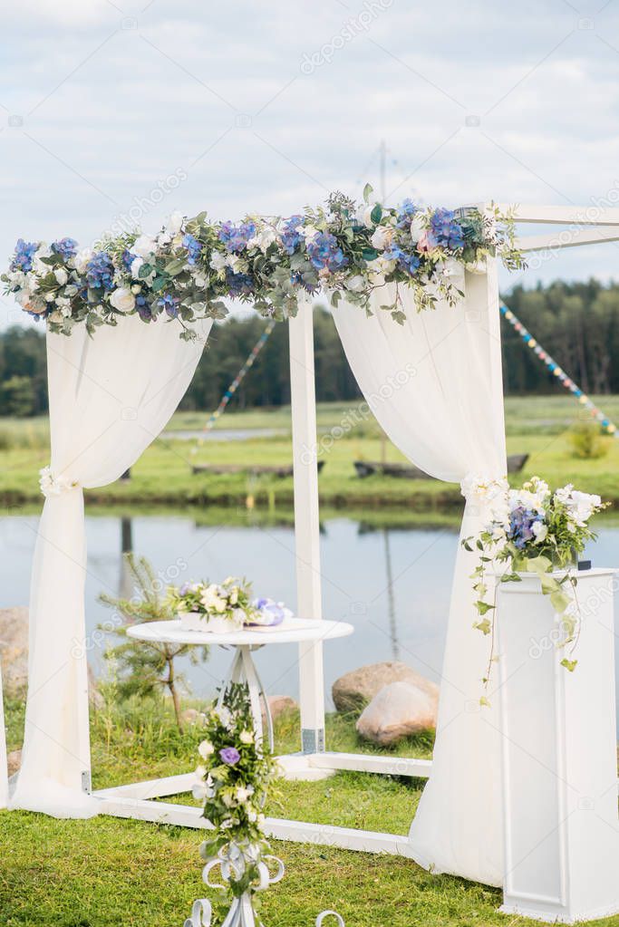 The wedding arch is decorated with blue flowers and white light silk. Summer Wedding Ceremony