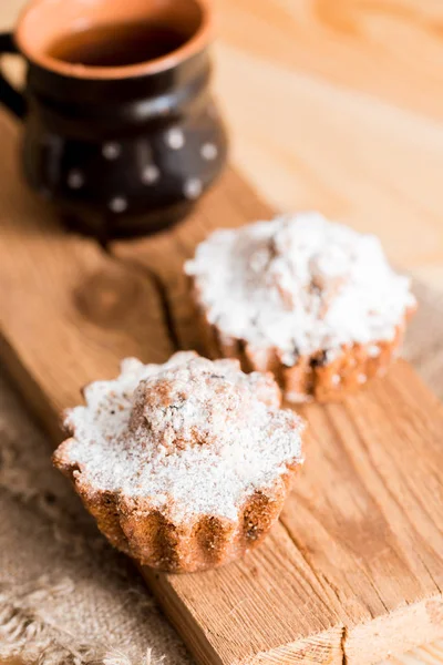 レーズンと粘土のカップで熱いお茶を春組成チョコレートのマフィン。ケーキの上の砂糖の粉。木製のテーブルの甘い朝食 — ストック写真