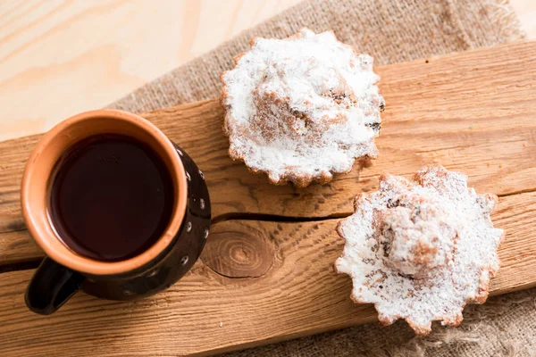 Composizione primaverile muffin al cioccolato con uvetta e tè caldo in una tazza di argilla. Zucchero in polvere sui dolci. Mattina colazione dolce su un tavolo di legno — Foto Stock