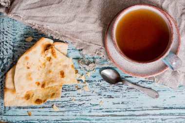 Bir fincan çay bir kil eski kupa, keten peçeteye bir ahşap mavi arka plan, waby sabi tarzında bir kuru düz kek rusk