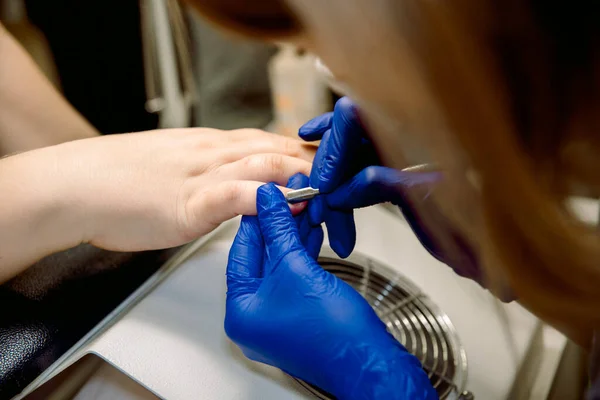 Manicure for a girl. Nail care in a beauty salon. Master removes shellac gel nails, which are exfoliated with sawing tool. — Stock Photo, Image