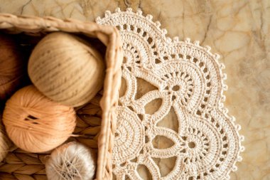 İplikler, örülmüş yuvarlak peçete. Çiçek gibi beyaz peçete. Mermer ışıklı arka planda. Hasır bir kutuda iplik topları. Rahat ev ve el yapımı konsept.