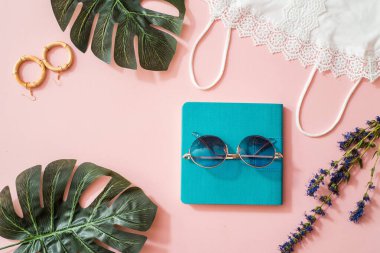 Üst te. Mavi defter ve lavanta çiçekleri. Plaj modası, yaz konsepti. Modaya uygun renkler. Moda gözlükleri, doğal pamuk openwork beyaz t-shirt, egzotik yaprakları.pembe arka plan