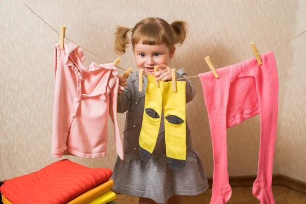 Menina engraçada com espinha de roupa e o varal. Roupa rosa bebê seca em uma corda. bebê pendura meias amarelas e uma camisola rosa. As tarefas domésticas. Conceito de limpeza dona de casa . — Fotografia de Stock