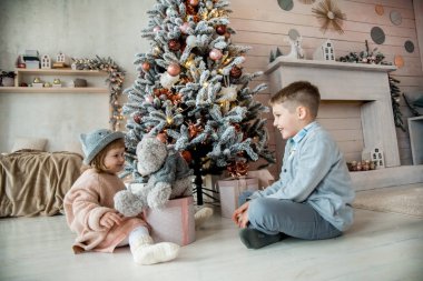 Noel 'de Noel ağacının altında oyuncak bir ayıyla aile. Çocuklar Noel hediyelerini hediye kutularıyla açıyorlar. Yeni yıl arifesinde Komin 'le aydınlık oturma odası. Evde sıcak bir kış akşamı.