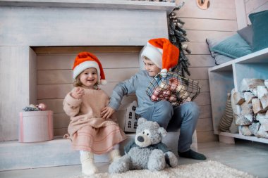 Noel 'de şöminenin yanında çocuklar, beyaz dekore edilmiş stüdyo, ev işçisi. Çocuklar San Claus 'dan hediyeler bekliyor. Yeni yıla az kaldı.