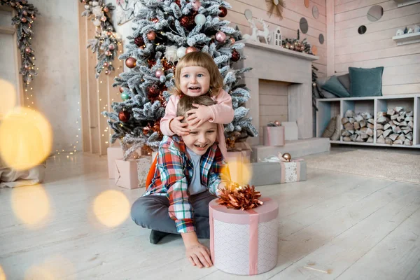Crianças em um estúdio de Natal decorado em cores pastel. Sala de estar brilhante, árvore de Natal, muitas luzes e bokeh. Crianças em chapéu vermelho de santa . — Fotografia de Stock