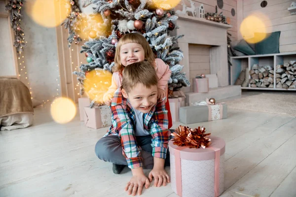 Crianças em um estúdio de Natal decorado em cores pastel. Sala de estar brilhante, árvore de Natal, muitas luzes e bokeh. Crianças em chapéu vermelho de santa . — Fotografia de Stock