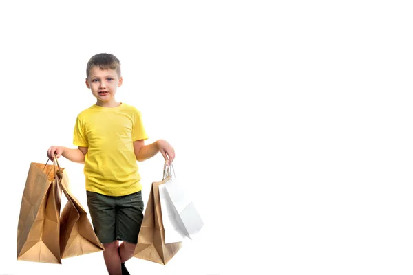 Glücklicher Junge mit Einkaufstaschen - vereinzelt weiß. leuchtend gelbes T-Shirt. Sommerschlussverkauf, schwarzer Freitag, Cyber-Montag. Große Umsätze für Kinderbastelpakete in der Hand. viele Einkäufe und Geschenke — Stockfoto