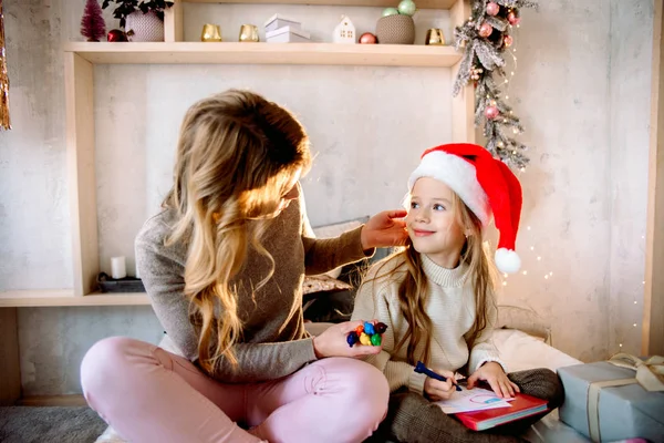 Vánoční dárky pro děti. v jasném penzionu na posteli šťastná rodina matka a dítě dcera napsat dopis Santa Claus na Vánoce . — Stock fotografie