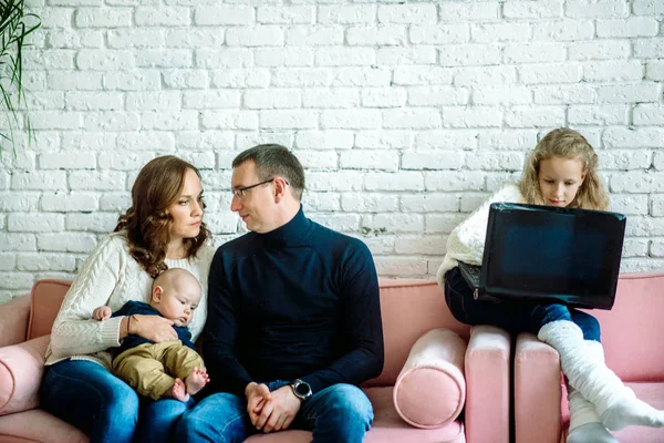 En casa en un sofá acogedor. padres cariñosos y hermano y hermana.Niña usando una computadora portátil con sus padres. El concepto de confrontación entre padres e hijos, adicción digital — Foto de Stock