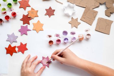 Bir çocuk kartondan bir yıldız oyuyor. Noel süsü, Noel çelengi, el yapımı ve sıfır atık. Beyaz arka planda bir çocuğun elleri. Div