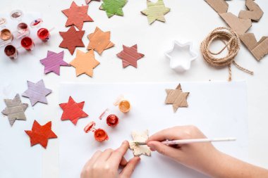 Bir çocuk kartondan bir yıldız oyuyor. Noel süsü, Noel çelengi, el yapımı ve sıfır atık. Beyaz arka planda bir çocuğun elleri. Div