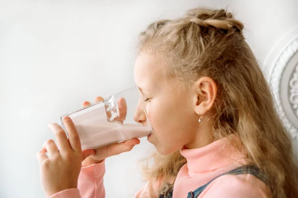 A rapariga bebe kefir ou leite ao pequeno-almoço. bigode engraçado. rindo no sofá em casa. alimentação saudável crianças — Fotografia de Stock