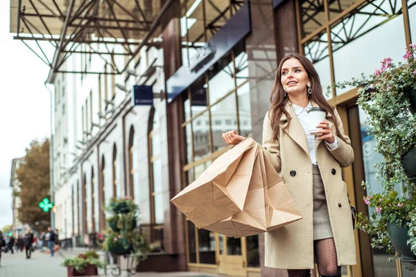 Mujer joven sosteniendo sacos de basura en la calle de la ciudad. Señora sonriente se ejecuta con grandes bolsas en la metrópoli. Consumismo, compras, ventas, concepto de estilo de vida —  Fotos de Stock