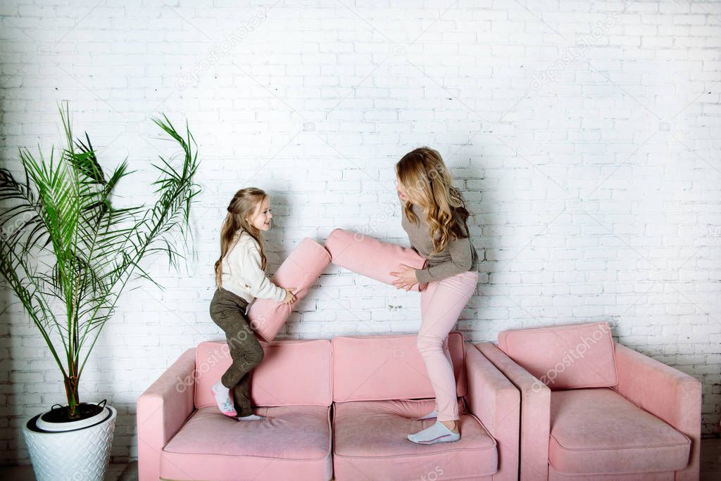 Parental love, upbringing and care.Happy mommy and kid daughter holding hands jumping on sofa together, baby sitter or mother playing having fun with cute kid girl at home
