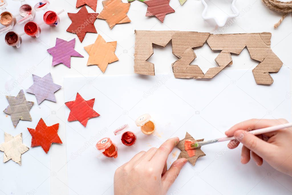 A child carves a star from cardboard. Christmas decoration, Christmas garland, hand made and Zero waste. Hands of a child on a white background. Div