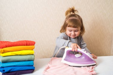 Bebek kız bebek kıyafetleri ütülüyor. Gökkuşağı gibi parlak kıyafetler yığını. Ev hanımı anneme yardım ediyor.
