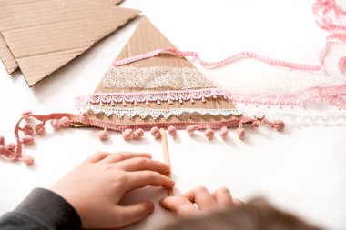 Çocuğun elinde Noel ağacı süsü var. Çocuklar için mutlu noel ağacı projesi. Pembe kurdeleler ve boncuklar. Beyaz arka planda karton ağaç. Sıfır Atık Kavramı.